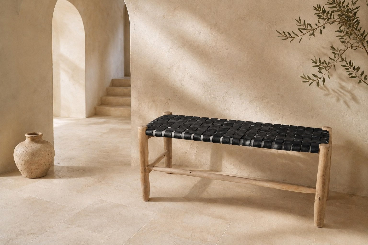 BAMA, banc en cuir tressé noir sur piètement de bois brut, dans une entrée en tadelakt